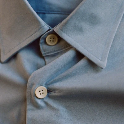 Macro detail of a pale blue oxford cotton shirt collar and button.