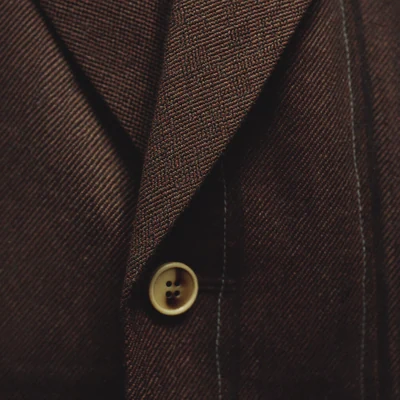 Macro detail of oxblood and charcoal Harris tweed herringbone with a horn button.